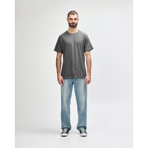 A grey adult t-shirt displayed on a male model, paired with black trousers and sneakers. The shirt has a logo.