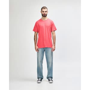 A coral Gildan Heavy Cotton Adult T-Shirt worn by a model, paired with black pants and casual sneakers.