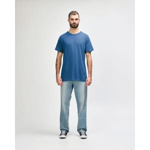A man stands wearing a blue Gildan Heavy Cotton adult t-shirt and black jeans, with a logo on the shirt.