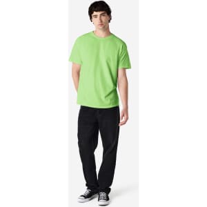 A man stands wearing a bright green Gildan Heavy Cotton adult T-shirt and black jeans, with a logo on the shirt.