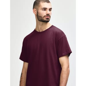 A maroon Gildan Heavy Cotton Adult T-Shirt displayed on a model with short, curly hair. The shirt has a logo.