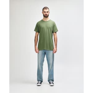 A green Gildan Heavy Cotton Adult T-Shirt, worn by a model paired with black jeans and sneakers, standing against a white background.