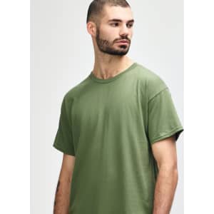 A man models a Gildan Heavy Cotton Adult T-Shirt in olive green, featuring a simple design and a logo.