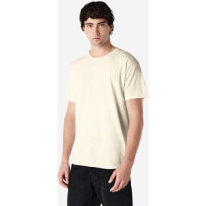 A man models a beige Gildan Heavy Cotton Adult T-Shirt, with a minimalistic design and short sleeves.