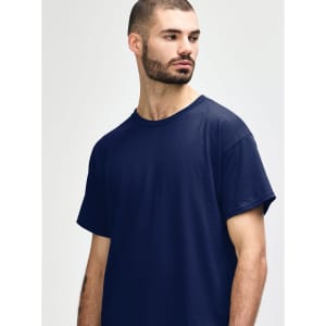 A navy Gildan Heavy Cotton adult T-shirt displayed on a model with short curly hair. The shirt has a simple design and branding.