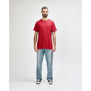 A red Gildan Heavy Cotton Adult T-Shirt worn by a model, paired with black jeans and sneakers. The shirt has a logo.