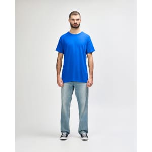 A man stands wearing a blue Gildan Heavy Cotton Adult T-Shirt paired with light blue jeans.