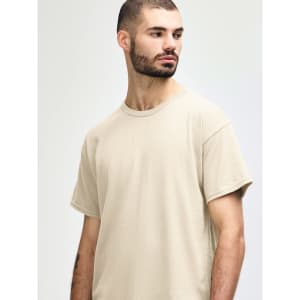 A beige Gildan Heavy Cotton Adult T-Shirt on a model, featuring a round neckline and a logo.