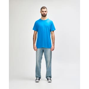 A blue Gildan Heavy Cotton adult t-shirt displayed on a model wearing black jeans and sneakers. The shirt has a logo.