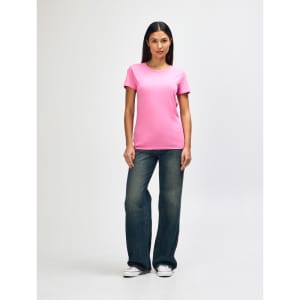 A pink Gildan Heavy Cotton Ladies' T-Shirt worn by a model paired with blue jeans and white sneakers.