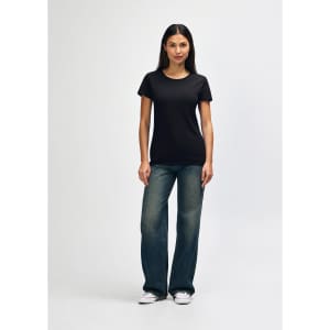 A black ladies' t-shirt displayed on a model, paired with blue jeans and white shoes, featuring a logo.