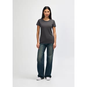 A woman wearing a dark grey Gildan Heavy Cotton ladies' T-shirt, paired with blue jeans and white sneakers.