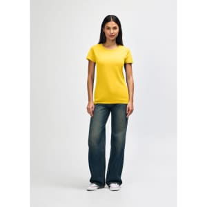 A woman wearing a yellow Gildan Heavy Cotton ladies' t-shirt paired with blue jeans and white sneakers.