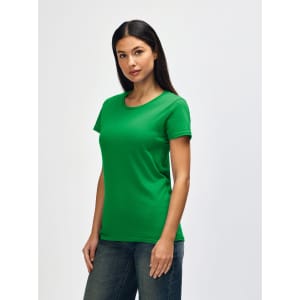 A woman wearing a green Gildan Heavy Cotton ladies' T-shirt, paired with blue jeans against a plain background.