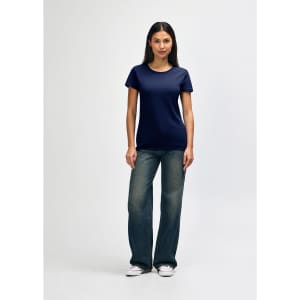 A model wearing a navy blue Gildan Heavy Cotton Ladies' T-Shirt paired with blue jeans and white sneakers.