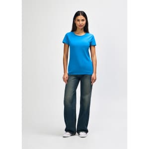 A woman wearing a bright blue Gildan Heavy Cotton Ladies' T-Shirt and jeans, standing against a plain background.