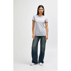 A grey ladies' T-shirt is worn by a model, paired with blue jeans and white sneakers. The shirt features a logo.