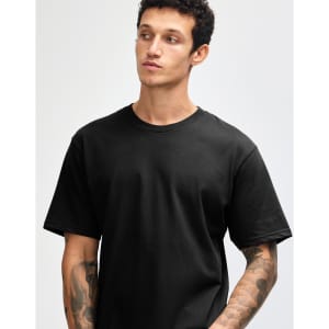 A black unisex short sleeve t-shirt displayed on a model with tattoos and a neutral expression.