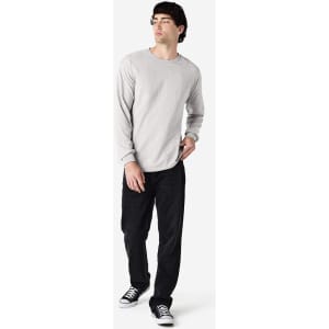 A long sleeve t-shirt in grey worn by a model, paired with black pants and sneakers, featuring a logo.