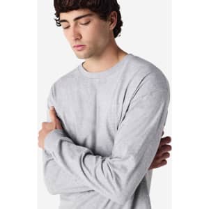 A grey long sleeve T-shirt worn by a model with arms crossed, featuring a simple design and logo.
