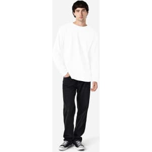 A model wearing a white long sleeve T-shirt with black jeans and sneakers, standing against a light background.