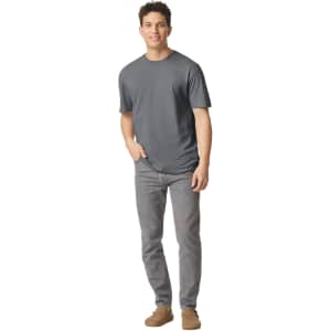A man stands wearing a grey Gildan Softstyle adult T-shirt paired with light grey jeans and casual footwear.