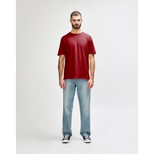 A model wearing a red Gildan Softstyle adult t-shirt paired with light blue jeans and white shoes. The shirt has a logo.