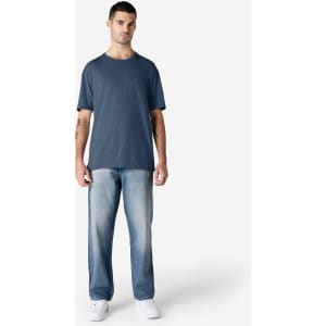 A model wearing a navy Gildan Softstyle adult T-shirt paired with light blue jeans and white shoes.
