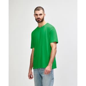 A green Gildan Softstyle adult T-shirt on a male model, paired with light denim jeans. The shirt has a logo.