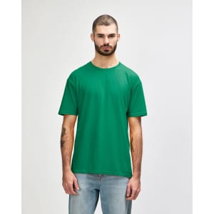 A man wearing a green Gildan Softstyle adult t-shirt, standing against a plain background, paired with blue jeans.