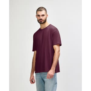 A maroon adult T-shirt displayed on a model, featuring a relaxed fit and short sleeves. Logo present.