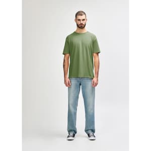 A man stands wearing an olive green Gildan Softstyle adult T-shirt paired with light blue jeans.