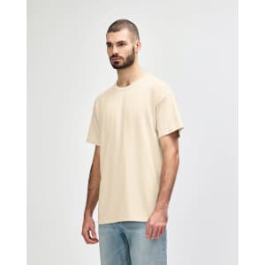 A beige Gildan Softstyle adult T-shirt features a relaxed fit and short sleeves, paired with light blue jeans.