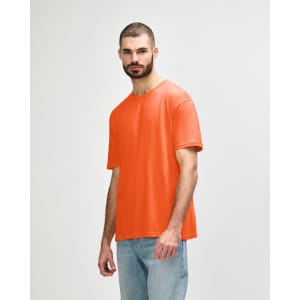 An orange Gildan Softstyle adult T-shirt displayed on a model wearing light blue jeans. The shirt features a logo.