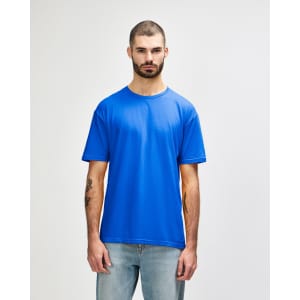 A man models a blue Gildan Softstyle adult t-shirt, paired with light denim jeans. The shirt has a logo.