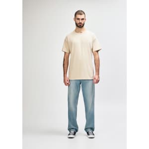 A light beige Gildan Softstyle adult T-shirt displayed on a model, paired with blue jeans. The model stands on a plain background.
