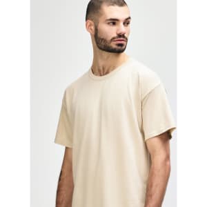 A light beige Gildan Softstyle adult T-shirt displayed on a model, featuring a relaxed fit and round neckline.