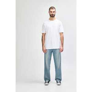 A man stands wearing a plain white Gildan Softstyle adult T-shirt paired with light blue jeans.