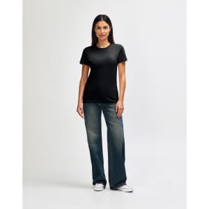 A model wears a black Gildan Softstyle ladies' T-shirt paired with blue jeans and white sneakers, showcasing a casual look.