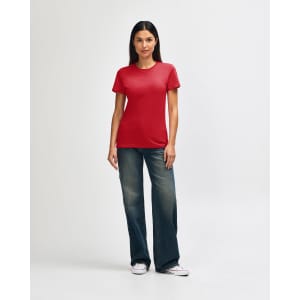 A red Gildan Softstyle ladies' t-shirt paired with blue jeans, worn by a woman standing against a plain background.