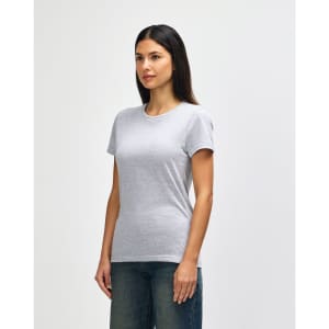 A grey Gildan Softstyle ladies' T-shirt, featured on a model, styled with blue jeans. The shirt has a logo.