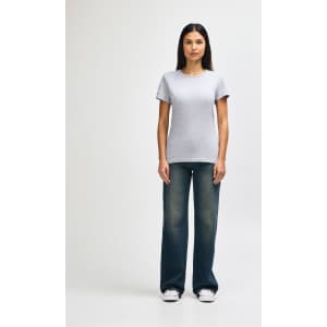 A grey ladies' t-shirt is worn with blue jeans and white sneakers, showcasing a casual outfit. The t-shirt has a logo.