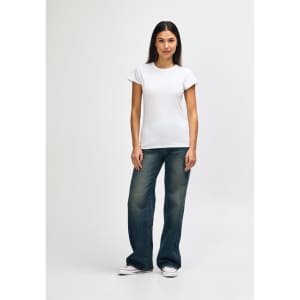 A model wearing a white Gildan Softstyle ladies' T-shirt paired with blue jeans and white sneakers.
