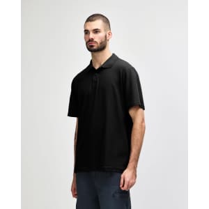 A model wearing a black Gildan Softstyle Adult Double Pique Polo, featuring a classic polo collar and short sleeves.