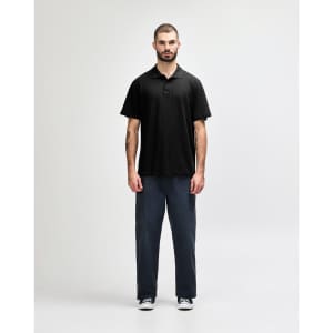 A model wearing a black Gildan Softstyle Adult Double Pique Polo, paired with dark jeans and sneakers.