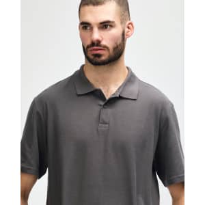 A model wearing a dark grey Gildan Softstyle Adult Double Pique Polo, featuring a classic collar and three-button placket.