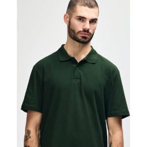 A model wearing a dark green Gildan Softstyle Adult Double Pique Polo with a three-button placket and collar.