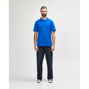 A model wears a blue Gildan Softstyle Adult Double Pique Polo with short sleeves, paired with light blue jeans.