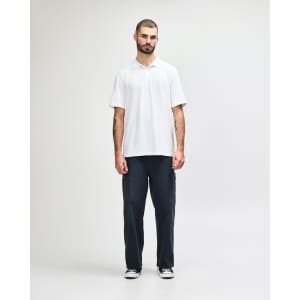 A model wearing a white Gildan Softstyle Adult Double Pique Polo paired with black pants and sneakers.