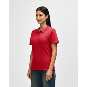 A red Gildan Softstyle Ladies' Double Pique Polo is displayed on a model, featuring a collar and short sleeves.